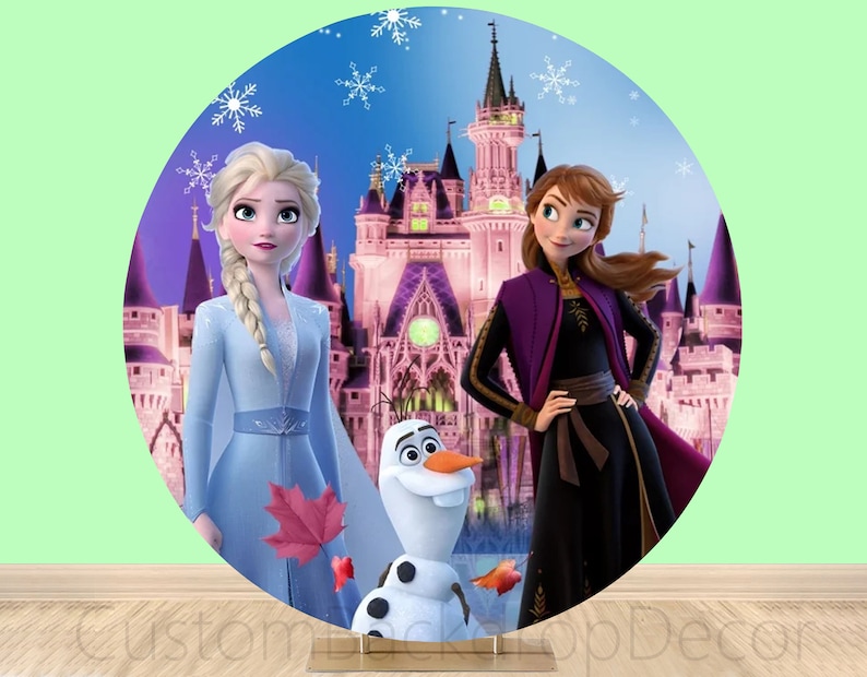 Puede incluir: Un tel&oacute;n de fondo redondo con un castillo rosa con dos princesas de la pel&iacute;cula Frozen. Elsa lleva un vestido azul claro y Anna lleva un vestido morado y negro. Olaf el mu&ntilde;eco de nieve est&aacute; de pie frente al castillo.
