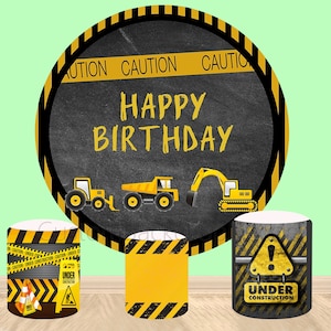 Puede incluir: Decoraciones de fiesta de cumpleaños con temática de construcción. Un gran telón de fondo redondo con cinta de precaución negra y amarilla y las palabras "Feliz cumpleaños" sobre un fondo de pizarra. Tres decoraciones redondas más pequeñas con cinta de precaución negra y amarilla y las palabras "En construcción".