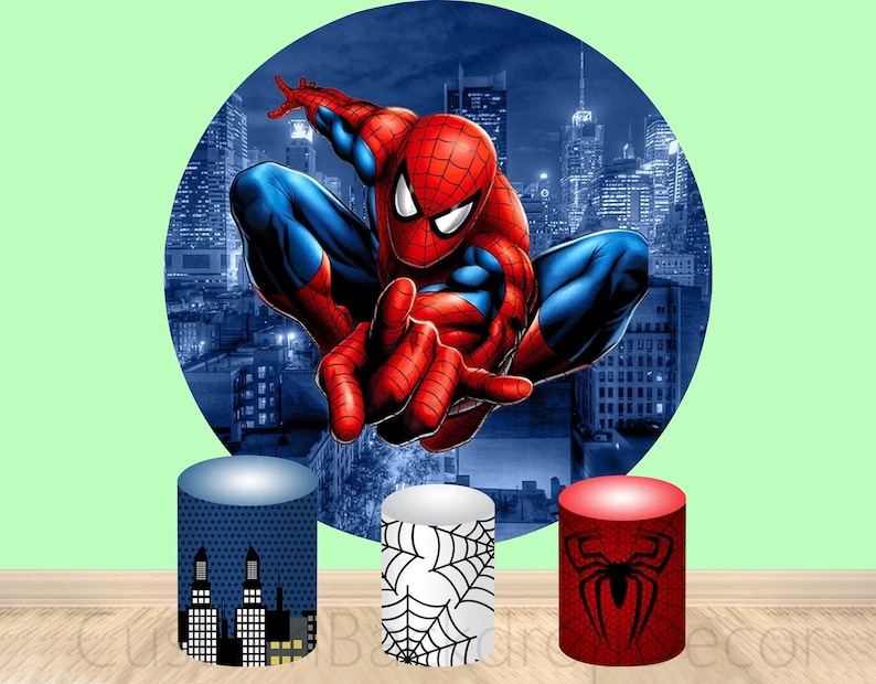 May include: Three round cardboard cake stands with different designs. The first stand is blue with a cityscape design. The second stand is white with a spiderweb design. The third stand is red with a black spider design. The background is a circular image of Spiderman swinging through a city.