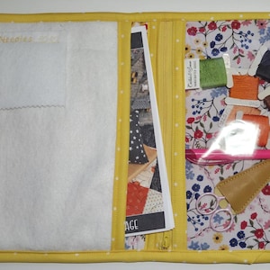 May include: A yellow fabric sewing organizer with white polka dots, featuring a white felt needle page, a central zipper pocket, and a right-side clear vinyl pocket containing colorful embroidery floss spools, a pink pen, and scissors.