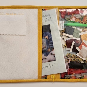 May include: A yellow fabric project organizer with a clear plastic pocket. The pocket contains embroidery floss, a needle, and a pattern with the text "Harvest Time" and "Grateful".