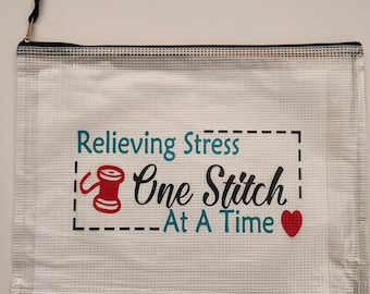 May include: A clear plastic zippered pouch with a white background and the text "Relieving Stress One Stitch At A Time" with a red heart and a red and white spool of thread graphic.