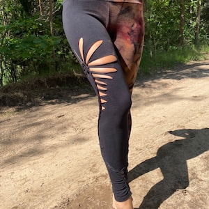 Op de afbeelding: Zwarte leggings met een tie-dye patroon op één been en een uitgesneden ontwerp op het andere been. De leggings zijn gemaakt van een zachte, rekbare stof.