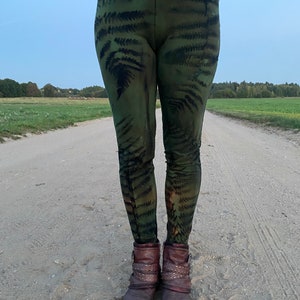 Könnte beinhalten: Grüne Leggings mit einem Farnmuster. Die Leggings sind aus einem weichen, dehnbaren Stoff und haben einen hohen Bund.