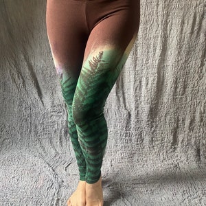 May include: Brown leggings with a green and white forest print. The print fades from brown to green and white.