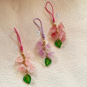 May include: Three pink flower charms with green leaves and gold accents on strings. The charms are numbered 1, 2, and 3.