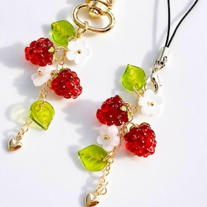 May include: Two charms featuring clusters of red raspberry-shaped beads, translucent green leaf-shaped beads, and small white five-petaled flowers. The charms are connected by gold-toned metal chains, with one featuring a gold lobster clasp.