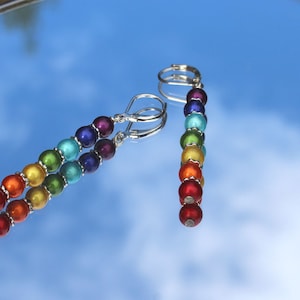 Peut inclure: Boucles d'oreilles pendantes en perles de verre arc-en-ciel avec crochets argentés. Les perles sont disposées en arc-en-ciel, en commençant par le rouge et en terminant par le violet.