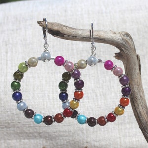 May include: A pair of silver hoop earrings with colorful beads. The beads are arranged in a rainbow pattern, with each bead a different color. The earrings are hanging from a silver hook.