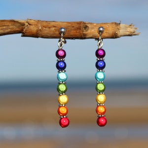 Peut inclure: Boucles d'oreilles pendantes en perles de couleur arc-en-ciel avec des crochets d'oreille en argent. Les perles sont irisées et ont une finition métallisée.