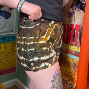 May include: Brown and white tie-dye shorts with a button on the side. The shorts are made of a lightweight fabric and have a relaxed fit.