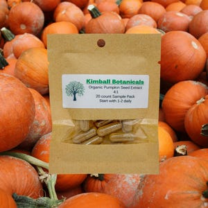 May include: A brown paper bag with a label that reads "Kimball Botanicals Organic Pumpkin Seed Extract 4:1 20 count Sample Pack Start with 1-2 daily". The bag contains a clear plastic bag with brown capsules inside. The bag is sitting on a pile of orange pumpkins.