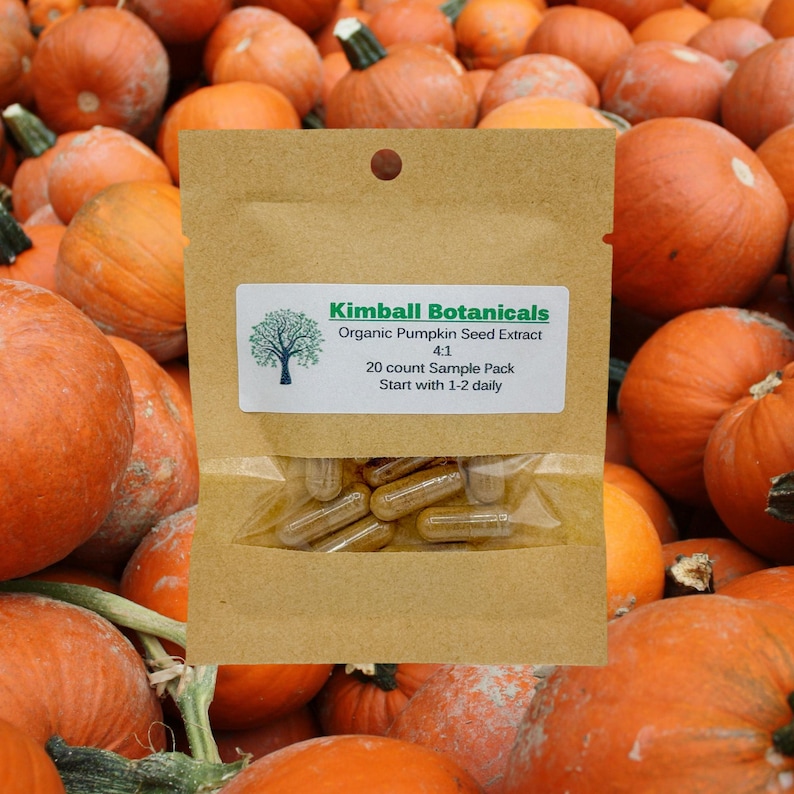 May include: A brown paper bag with a label that reads "Kimball Botanicals Organic Pumpkin Seed Extract 4:1 20 count Sample Pack Start with 1-2 daily". The bag contains a clear plastic bag with brown capsules inside. The bag is sitting on a pile of orange pumpkins.