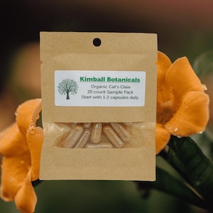Pu&ograve; includere: Un piccolo sacchetto di carta marrone con un'etichetta bianca che recita "Kimball Botanicals Organic Cat's Claw 20 count Sample Pack Start with 1-2 capsules daily". Il sacchetto contiene un campione di capsule.