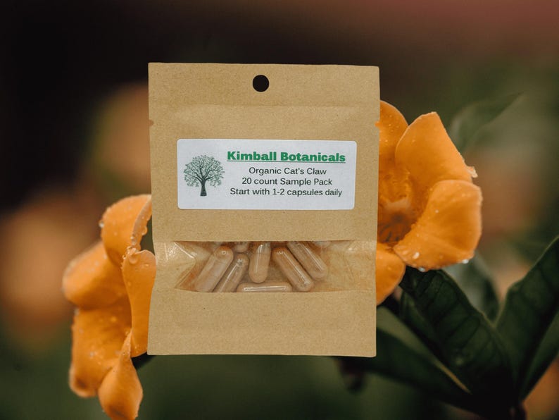 Pu&ograve; includere: Un piccolo sacchetto di carta marrone con un'etichetta bianca che recita "Kimball Botanicals Organic Cat's Claw 20 count Sample Pack Start with 1-2 capsules daily". Il sacchetto contiene un campione di capsule.
