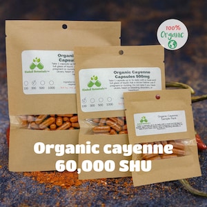 May include: Three brown paper bags with different sizes containing organic cayenne capsules. The bags have a label with the text "Kimball Botanicals" and "Organic Cayenne Capsules". The largest bag has a label that says "Organic Cayenne Capsules 500mg". The smallest bag has a label that says "Organic Cayenne Sample Pack". The text "Organic cayenne 60,000 SHU" is written in large letters below the bags.