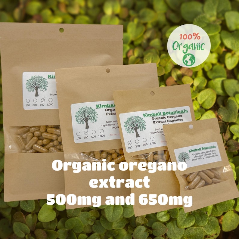 May include: Several brown paper bags of organic oregano extract capsules are displayed against a green leafy background. The bags have white labels with a tree logo and the text "Kimball Botanicals." The text "Organic oregano extract 500mg and 650mg" is also visible.