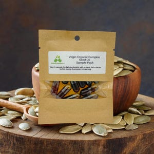 May include: A brown paper pouch with a clear window showing a sample pack of dark brown capsules filled with virgin organic pumpkin seed oil. The pouch has a white label with the text "Virgin Organic Pumpkin Seed Oil Sample Pack". The text "Take 1 capsule 2x daily preferably with a meal. Ask a doctor before taking if pregnant or nursing" is also on the label.