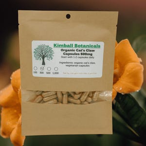 Pu&ograve; includere: Un sacchetto di carta marrone con un'etichetta bianca che recita "Kimball Botanicals Organic Cat's Claw Capsules 500mg Start with 1-2 capsules daily Ingredients: organic cat's claw, vegetarian capsules 100 300 500 1,000". Il sacchetto contiene capsule.
