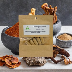 May include: A small brown paper bag with a white label that reads "Organic Tri Mushroom Blend Sample Pack". The bag contains several capsules. The bag is surrounded by dried mushrooms.