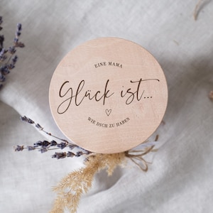 Könnte beinhalten: Ein rundes Holzschild mit dem Text "Eine Mama Glück ist... Wie dich zu haben" und einem kleinen Herzsymbol.