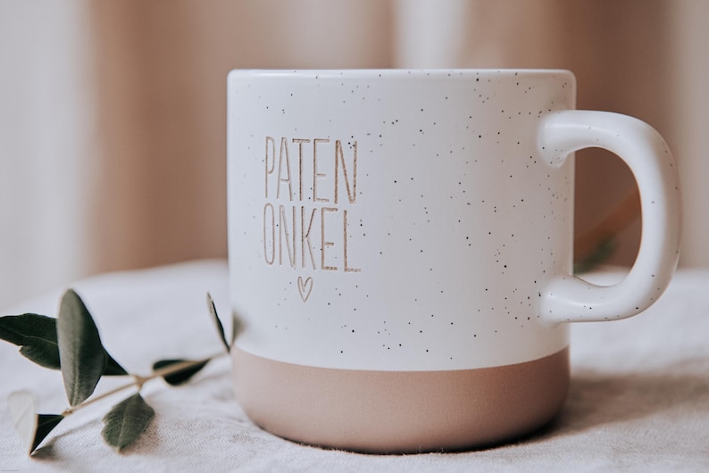 Gravierte Keramiktasse mit modernem Steingutdesign  weißer matter Lasur und kleinen sprenkeln der Oberfläche und unglasiertem Bodendesign in Natur. Im Detailbild werden die ungleichmäßigen Sprenkel der Tasse sichtbar.