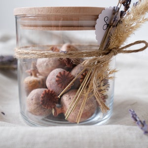 Hochwertiges Glasgefäß mit Holzdeckel, gefüllt mit natürlichem Potpourri. Dekoratives Seil umschließt das Glas, kombiniert mit zarten, getrockneten Blumen. Perfekt für eine gemütliche Atmosphäre in Ihrem Zuhause. Ideal als stilvolles Geschenk oder als elegantes Dekorelement, das Wärme und Naturverbundenheit ausstrahlt.