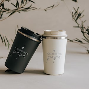 Zwei stylische Thermobecher mit der Aufschrift "Weltbester Papa" stehen auf einem Tisch. Der eine Becher ist in elegantem Schwarz, der andere in modernem Weiß gestaltet. Diese Becher sind das perfekte Geschenk, um Wertschätzung und Wärme auszudrücken. Ideal für jeden Vater, der seinen Kaffee unterwegs genießen möchte und stets an die Liebe seiner Familie erinnert werden will.