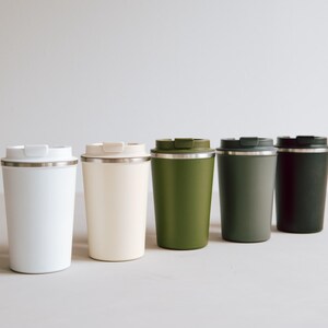 Stilvolle, umweltfreundliche Thermobecher in sanften Naturtönen stehen in einer eleganten Reihe. Perfekt für Ihren täglichen Kaffee oder Tee unterwegs. Genießen Sie jede Schluck mit modernem Design und halten Sie Ihr Getränk stundenlang heiß oder kalt. Diese Becher vereinen Funktionalität mit Ästhetik und sind ein Muss für jeden umweltbewussten Lifestyle-Liebhaber.
