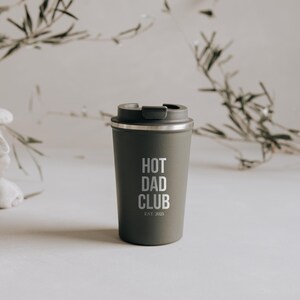 Stylischer, olivgrüner Thermobecher mit "Hot Dad Club"-Aufschrift, perfekt für trendbewusste Väter. Der Becher vereint modernes Design mit Funktionalität und hält Getränke stundenlang warm. Ein Must-Have für alle, die Wert auf Stil und Nachhaltigkeit legen. Ideal als Geschenk oder persönliches Statement für unterwegs.