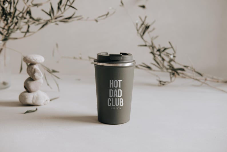 Stylischer, olivgrüner Thermobecher mit "Hot Dad Club"-Aufschrift, perfekt für trendbewusste Väter. Der Becher vereint modernes Design mit Funktionalität und hält Getränke stundenlang warm. Ein Must-Have für alle, die Wert auf Stil und Nachhaltigkeit legen. Ideal als Geschenk oder persönliches Statement für unterwegs.