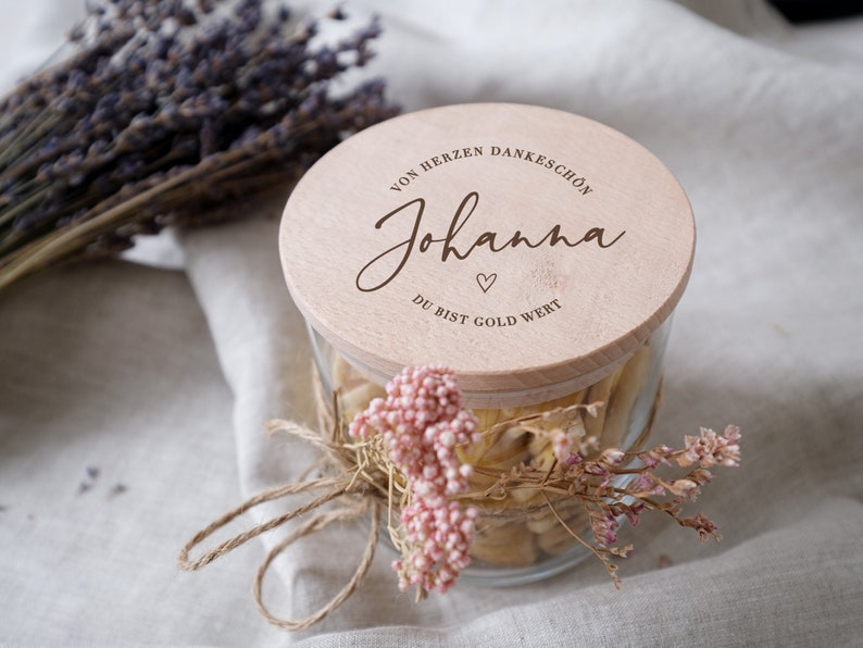 Liebevoll gestaltetes Glas mit personalisiertem Holzdeckel, verziert mit zarten Trockenblumen und einer natürlichen Jutekordel. Ein perfektes Geschenk, um Dankbarkeit auszudrücken und eine besondere Verbindung zu feiern. Ideal als individuelle Aufmerksamkeit für besondere Anlässe, die Herzen höher schlagen lässt und ein Lächeln zaubert.