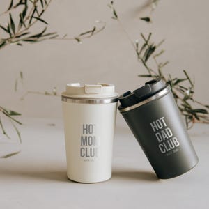 Zwei stilvolle Thermobecher mit den Aufschriften "Hot Mom Club" und "Hot Dad Club", perfekt für Eltern, die ihren Kaffee unterwegs genießen möchten. Diese eleganten Becher aus hochwertigen Materialien halten Getränke heiß und sind ideal für den modernen Lifestyle. Ein Must-have für alle, die Funktionalität und Design schätzen. Perfektes Geschenk für trendbewusste Eltern.