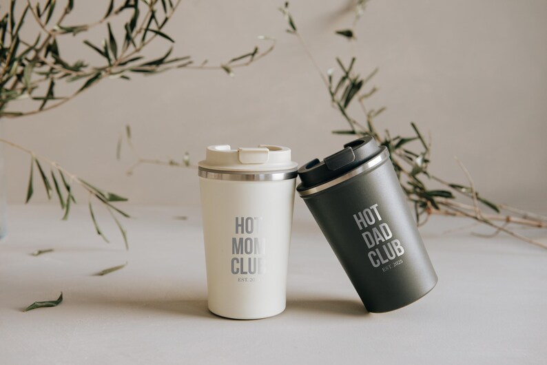 Zwei stilvolle Thermobecher mit den Aufschriften "Hot Mom Club" und "Hot Dad Club", perfekt für Eltern, die ihren Kaffee unterwegs genießen möchten. Diese eleganten Becher aus hochwertigen Materialien halten Getränke heiß und sind ideal für den modernen Lifestyle. Ein Must-have für alle, die Funktionalität und Design schätzen. Perfektes Geschenk für trendbewusste Eltern.