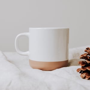 Steinguttasse gin Nahaufnahme mit glanzweiß in einer gemütliche Atmosphäre  – Tasse mit glänzender Lasur der Oberfläche und unglasiertem Bodendesign in Natur, individuell anpassbar nach euren wünschen.