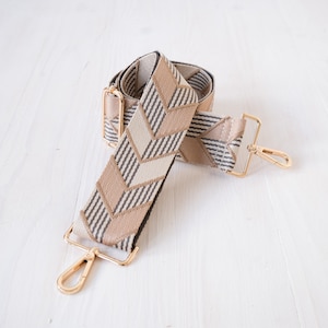 May include: A beige and brown patterned adjustable strap with gold metal hardware and clasps.