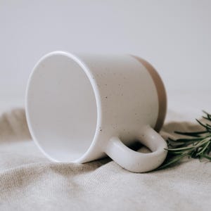 Liegende Keramiktasse im Steingutdesign zeigt die matte Lasur und kleinen Sprenkler der Oberfläche und unglasiertem Bodendesign in Natur, Innen ist die Tasse mit der Lasur durchgefärbt.