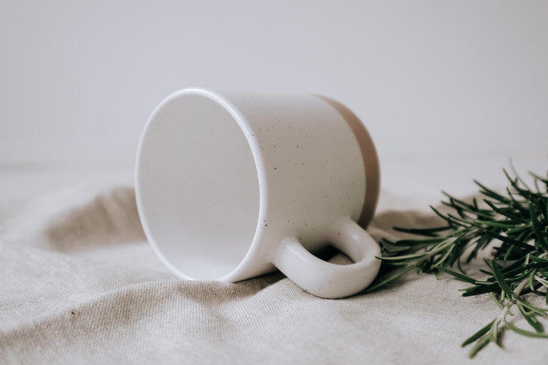 Liegende Keramiktasse im Steingutdesign zeigt die matte Lasur und kleinen Sprenkler der Oberfläche und unglasiertem Bodendesign in Natur, Innen ist die Tasse mit der Lasur durchgefärbt.