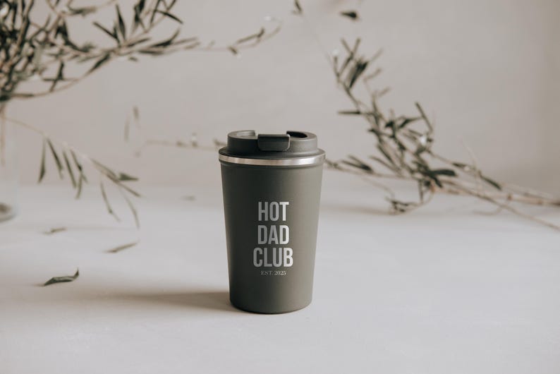 Stylischer Thermobecher mit der Aufschrift "Hot Dad Club" vor elegantem, natürlichem Hintergrund. Perfekt für den modernen Vater, der unterwegs seinen Kaffee stilvoll genießen möchte. Hält Getränke heiß und verleiht jedem Morgen einen Hauch von Coolness. Ein ideales Geschenk für Väter, die Wert auf Design und Funktionalität legen.