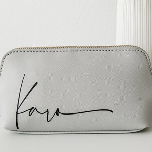 Nahaufnahme von Kulturtasche in grau mit verschnörkelter schwarzer Schrift