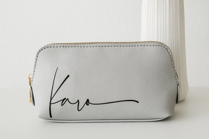 Nahaufnahme von Kulturtasche in grau mit verschnörkelter schwarzer Schrift