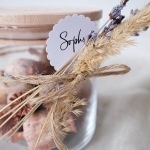 Dekoriertes Vorratsglas mit graviertem Holzdeckel und Trockenblumen als Deko. Kann Spuren von Glück enthalten.