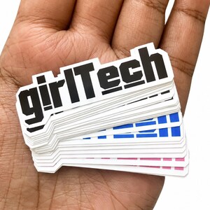 May include: A stack of die-cut vinyl stickers featuring the text girlTech in a bold, black, sans-serif font. The stickers are layered, revealing different colors on the bottom edges, including blue and pink, against a white background.