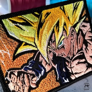 May include: Embroidered patch depicting a character with spiky yellow hair, green eyes, and a determined expression. The patch has a black border and an orange and yellow background, with blue detailing.