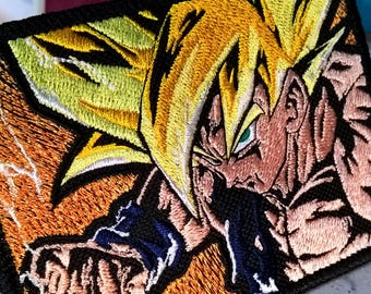 May include: Embroidered patch depicting a character with spiky yellow hair, green eyes, and a determined expression. The patch has a black border and an orange and yellow background, with blue detailing.