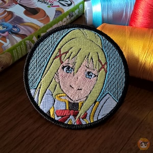 May include: Embroidered patch featuring a cartoon anime character with blonde hair, blue eyes, and a red bow. The character is wearing a white and blue outfit. The patch is circular and has a black border.