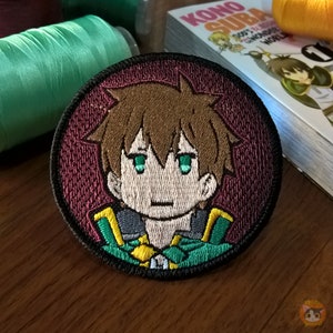 Puede incluir: Un parche redondo bordado con un personaje de dibujos animados con cabello castaño, ojos verdes y un atuendo verde y dorado. El parche tiene un fondo burdeos y un borde negro.