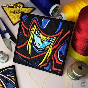 Peut inclure: Écusson carré brodé noir représentant un personnage aux cheveux jaunes, aux yeux bleus et vêtu de bleu et de rouge. L'écusson est entouré de bobines de fil bleu, jaune et rouge, ainsi que d'un charm doré et de ciseaux.