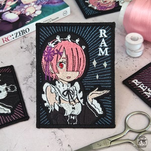Puede incluir: Parche bordado con un personaje de anime de dibujos animados con cabello rosado, que lleva un vestido de sirvienta blanco. El personaje está rodeado de un fondo azul y negro con la palabra "RAM" en letras blancas.