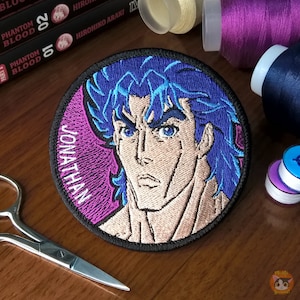May include: A round embroidered patch featuring a portrait of Jonathan Joestar from the anime series JoJo's Bizarre Adventure. The patch has a black border, a pink background, and a blue and white image of Jonathan Joestar.